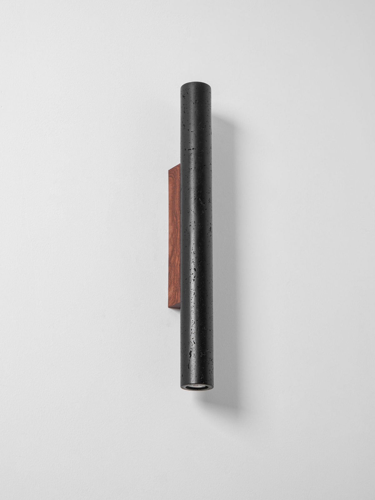 A tall, narrow Clérachic black cylinder on a walnut plate, switched off, seen at an angle against a pale wall.