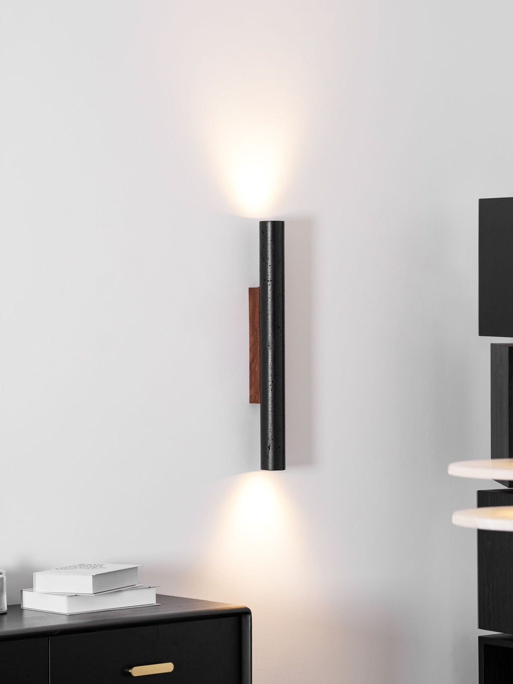 A tall Clérachic wall light shines up and down beside black shelving and a black sideboard with brass handles.