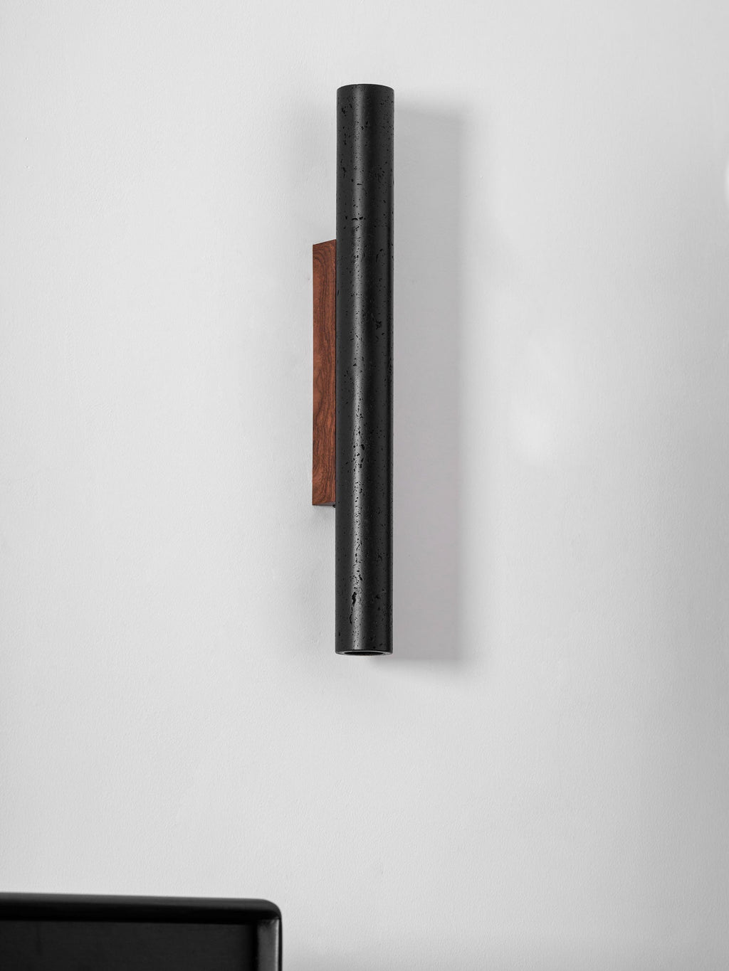 Side view of a tall black Clérachic cylinder and its walnut backplate on a white wall, unlit.