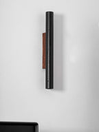 Side view of a tall black Clérachic cylinder and its walnut backplate on a white wall, unlit.