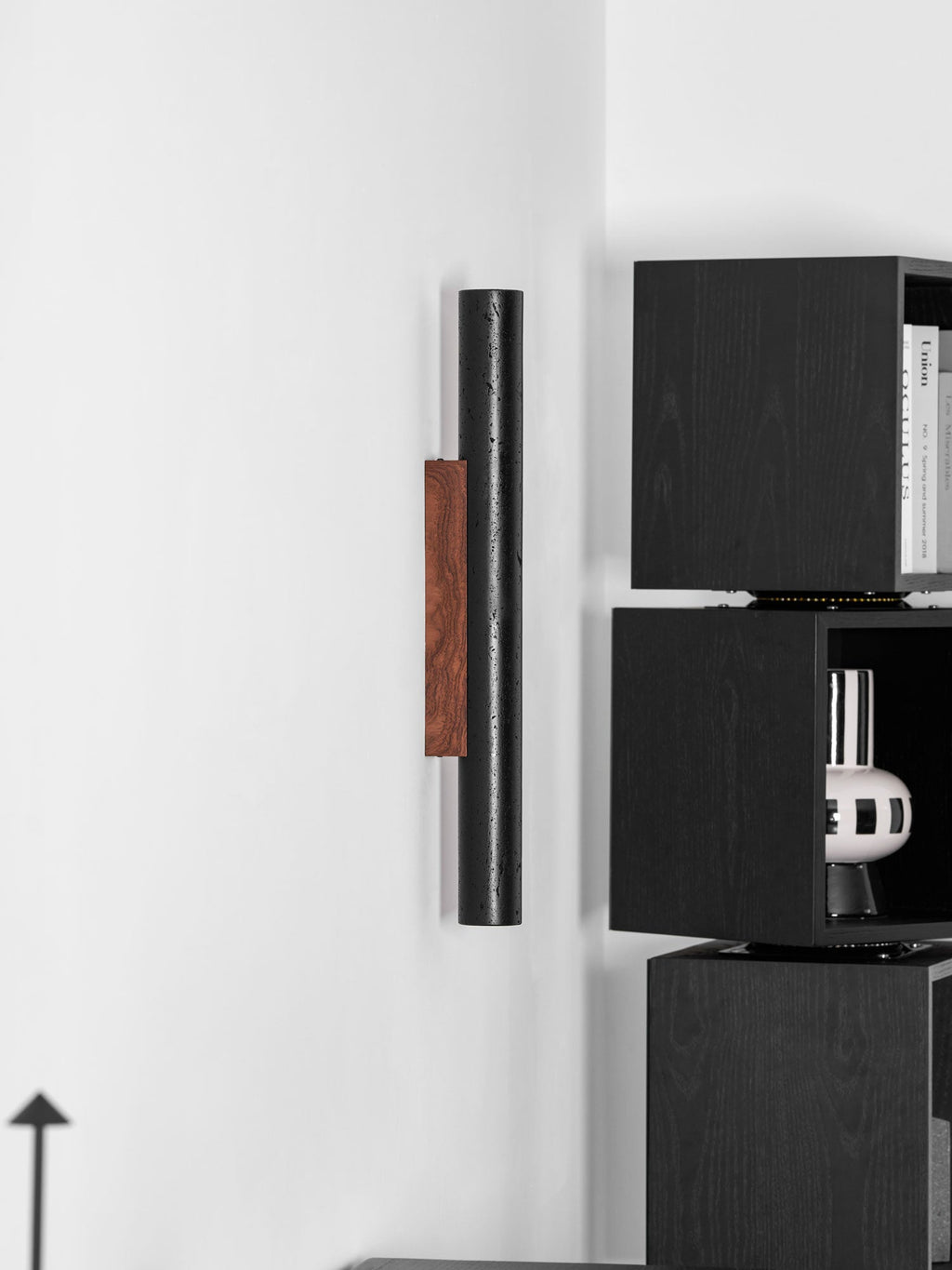 A tall Clérachic black cylinder with a walnut plate stands out on a white wall beside a stack of dark open shelves.