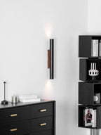 A slender Clérachic wall light glows softly up and down above a black chest of drawers and a small cordless lamp.