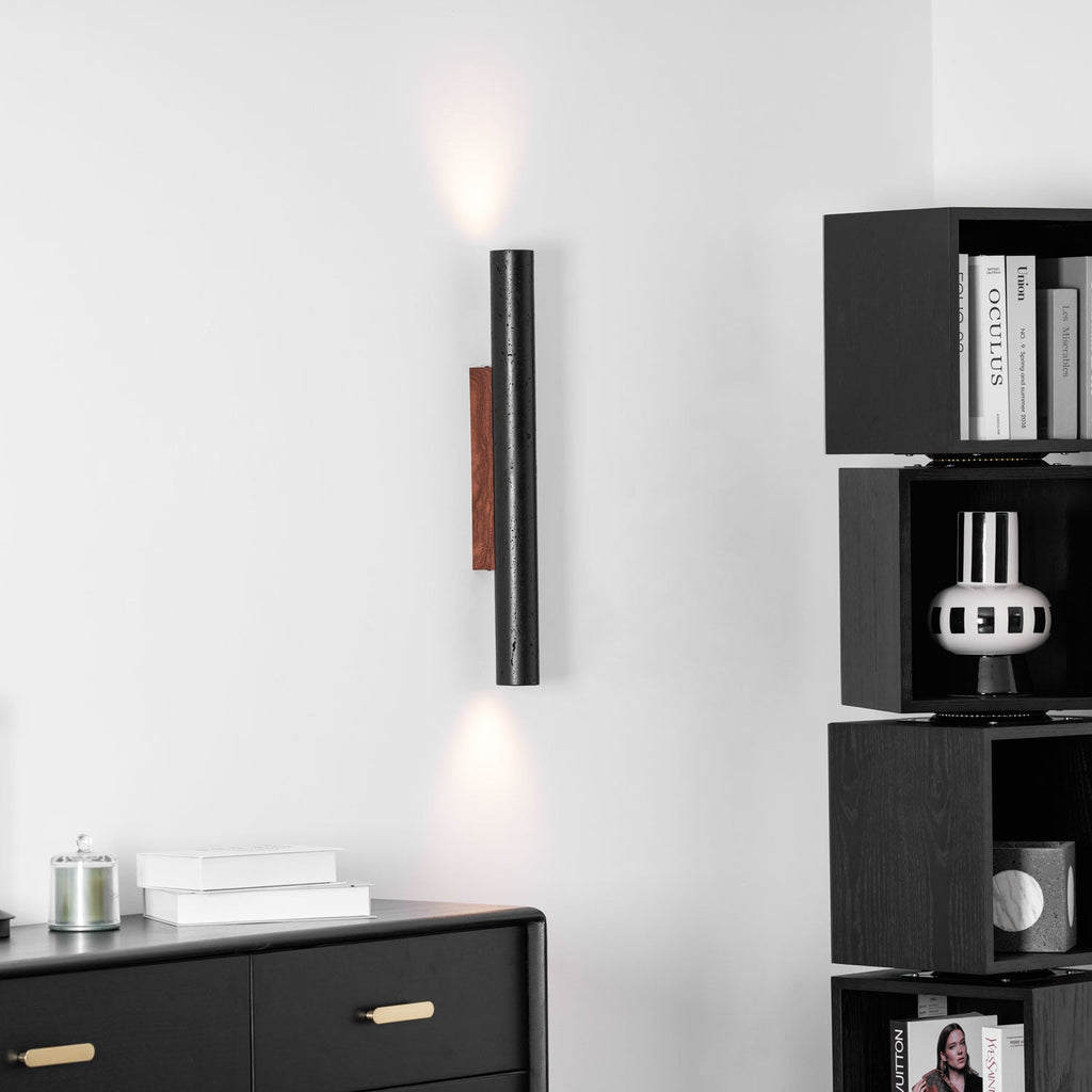 A slim Clérachic wall light lit at both ends, next to black cube shelving and above a drawer unit and stacked books.