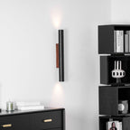 A slim Clérachic wall light lit at both ends, next to black cube shelving and above a drawer unit and stacked books.