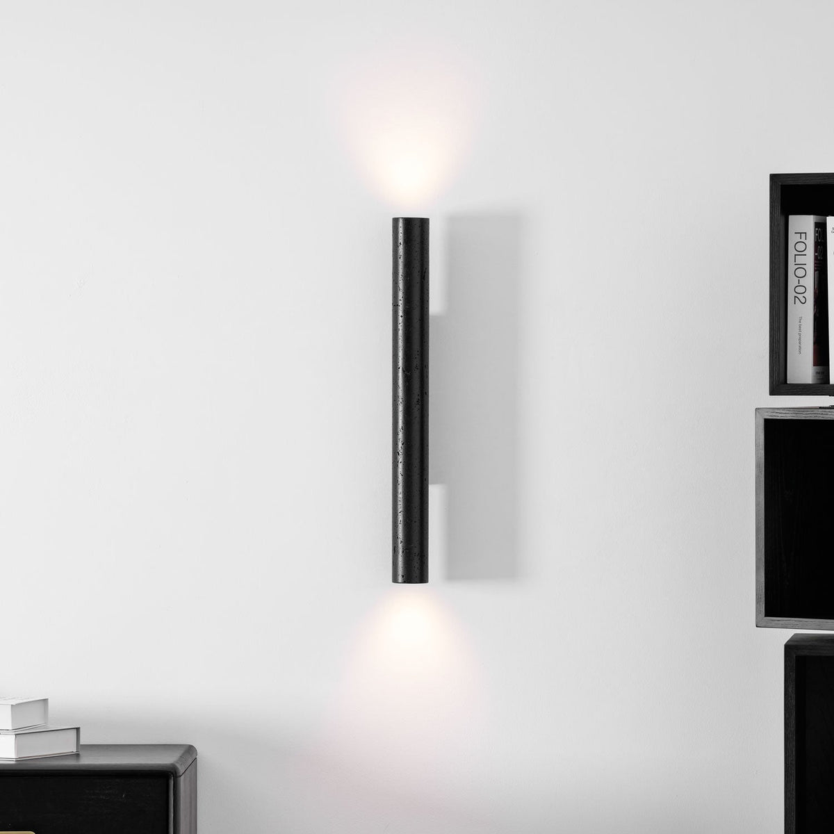 A tall Clérachic cylinder wall light fills the wall above and below with soft light, with dark shelves at the edge.