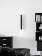 A tall Clérachic cylinder wall light with a soft up and down glow, above a black armchair and a chest with brass pulls.