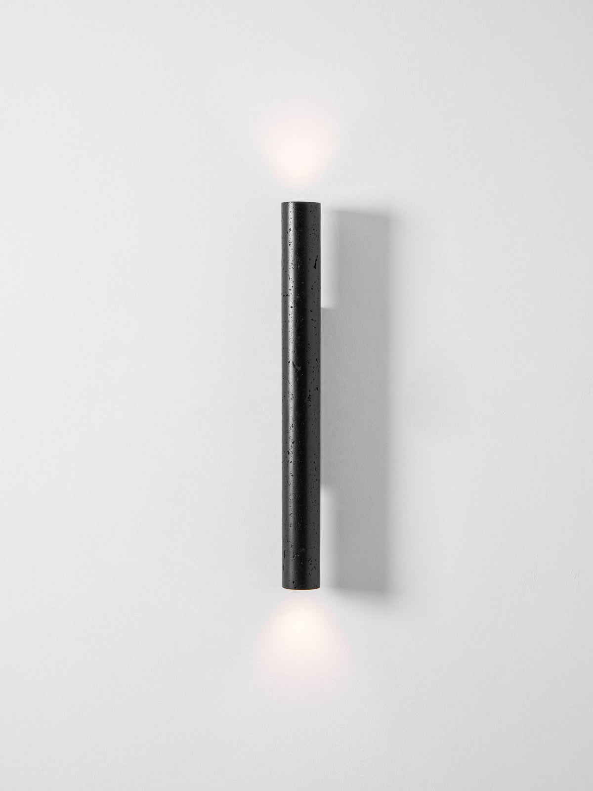 A tall Clérachic wall light throws a faint glow above and below it on a pale, clean wall.