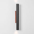 A tall Clérachic black stone cylinder with a walnut backplate, with light just visible at the top and bottom edges.