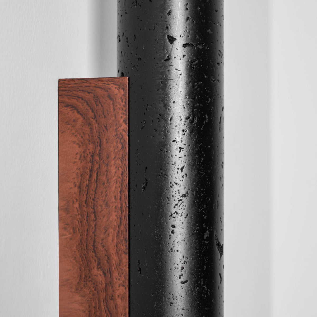 Close view of the walnut grain on the backplate beside the pitted black travertine of this Clérachic wall light.