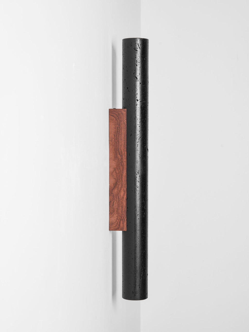 Angled view of a tall Clérachic black cylinder, its walnut backplate standing proud of the white wall, unlit.