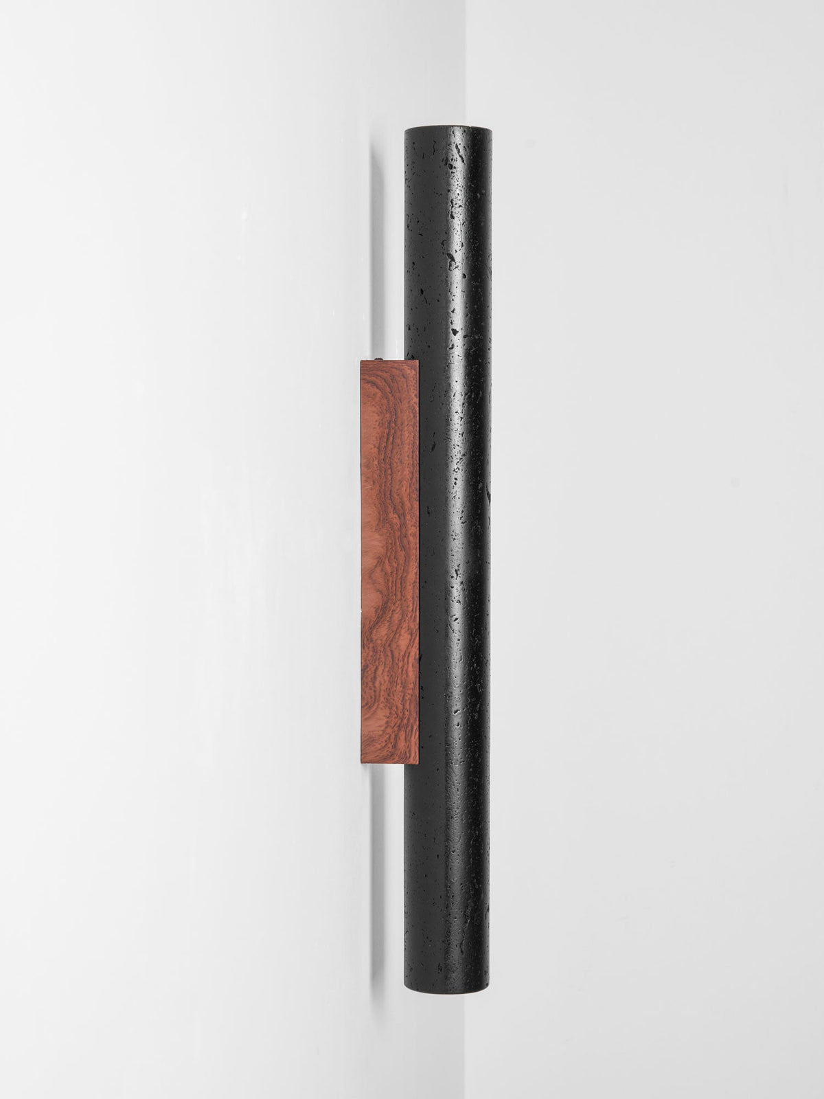 Angled view of a tall Clérachic black cylinder, its walnut backplate standing proud of the white wall, unlit.