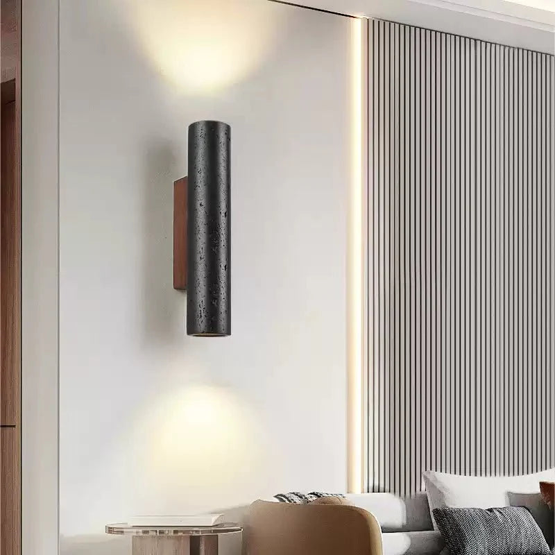 A Clérachic black stone wall light glows up and down above a lounge with a ribbed wall panel and cushions.
