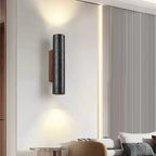 A Clérachic black stone wall light glows up and down above a lounge with a ribbed wall panel and cushions.