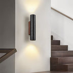 A Clérachic cylinder wall light casts light up and down a white wall beside a dark timber staircase.
