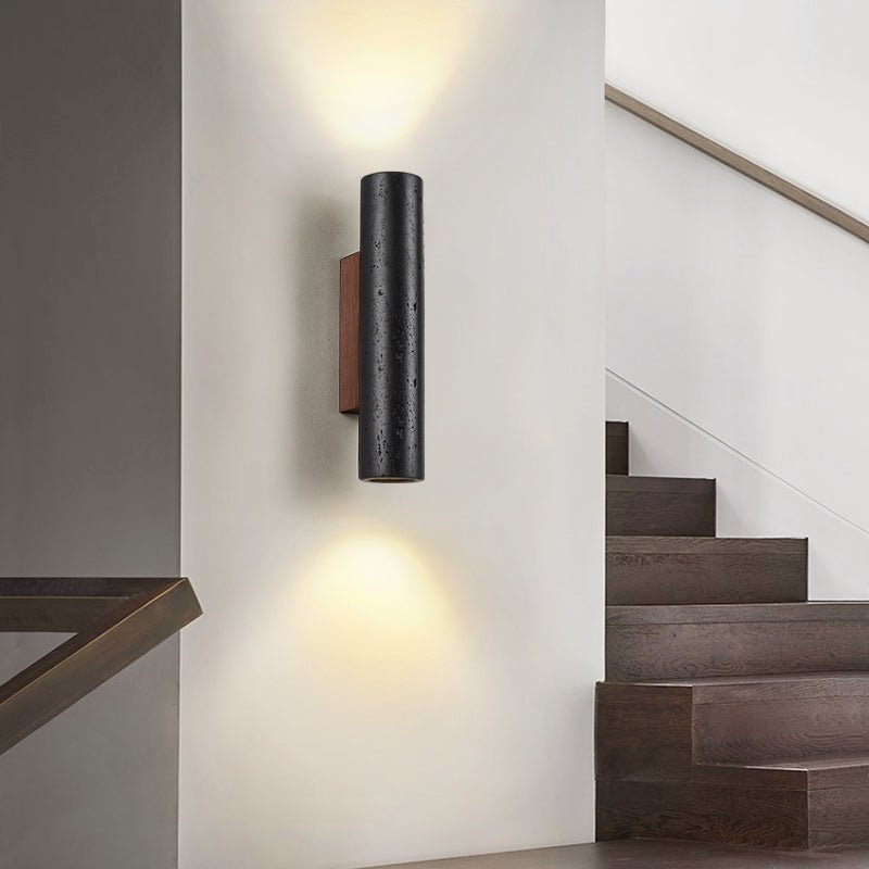 A Clérachic cylinder wall light casts light up and down a white wall beside a dark timber staircase.