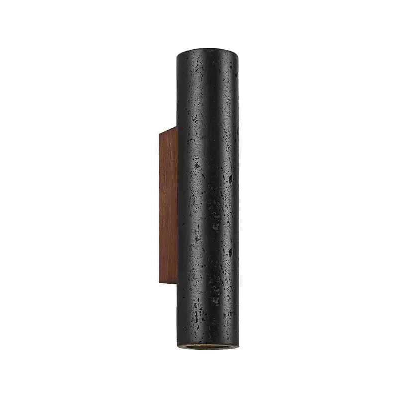 A black travertine cylinder on a walnut plate, unlit, in a Clérachic wall light shown against a plain white backdrop.