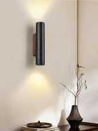 A Clérachic black stone wall light throws light above and below, over a dark vase with a branch and a low table.