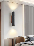 A Clérachic wall light glows up and down in a bedroom with a ribbed wall panel, a camel chair and a bedside table.