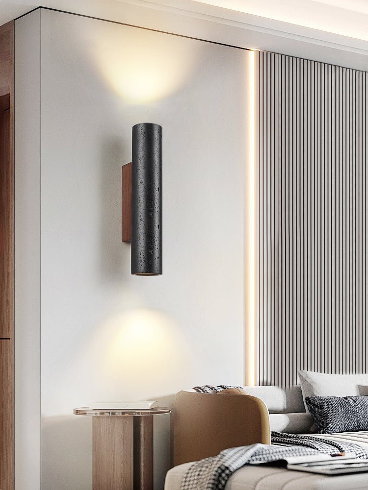A Clérachic wall light glows up and down in a bedroom with a ribbed wall panel, a camel chair and a bedside table.