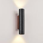 A close, angled view of a Clérachic wall light, its pitted black stone lit above and below on a pale wall.