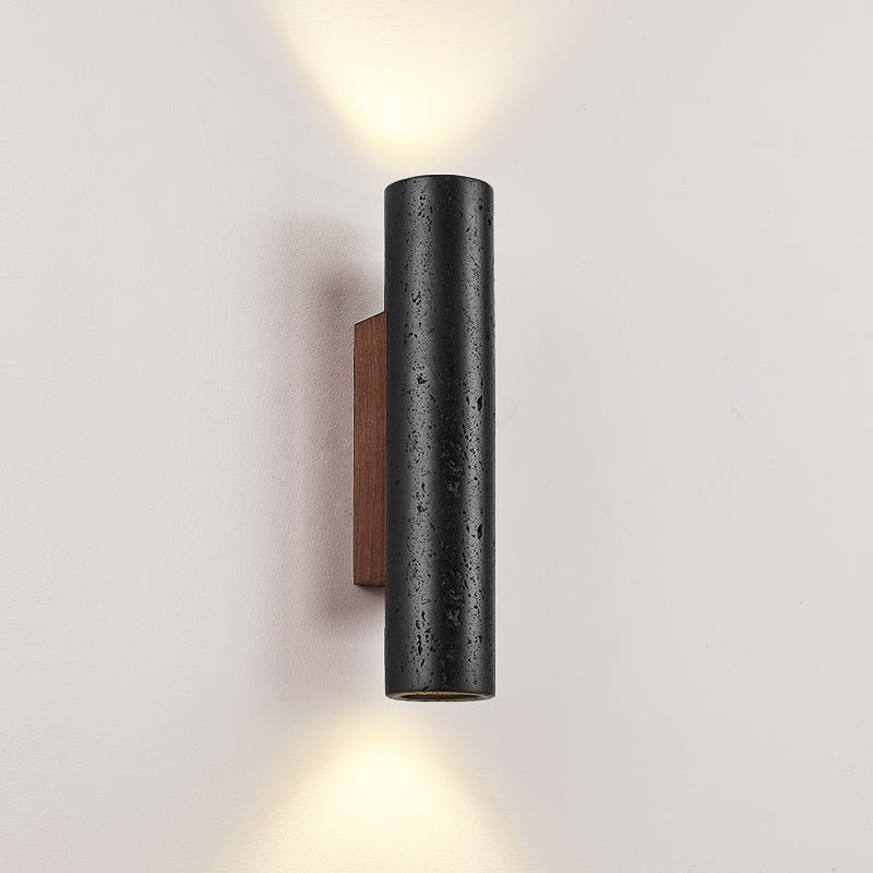 A close, angled view of a Clérachic wall light, its pitted black stone lit above and below on a pale wall.
