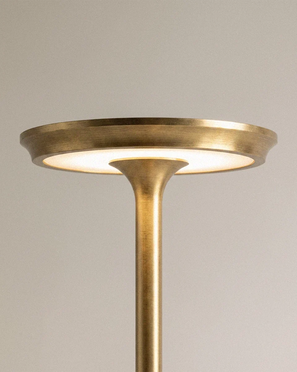 A close view of the Clérachic gold lamp's saucer-shaped top reveals its warm glowing LED disc.