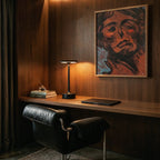 A lit Clérachic black table lamp sits on a walnut desk beside stacked books and a framed portrait painting.