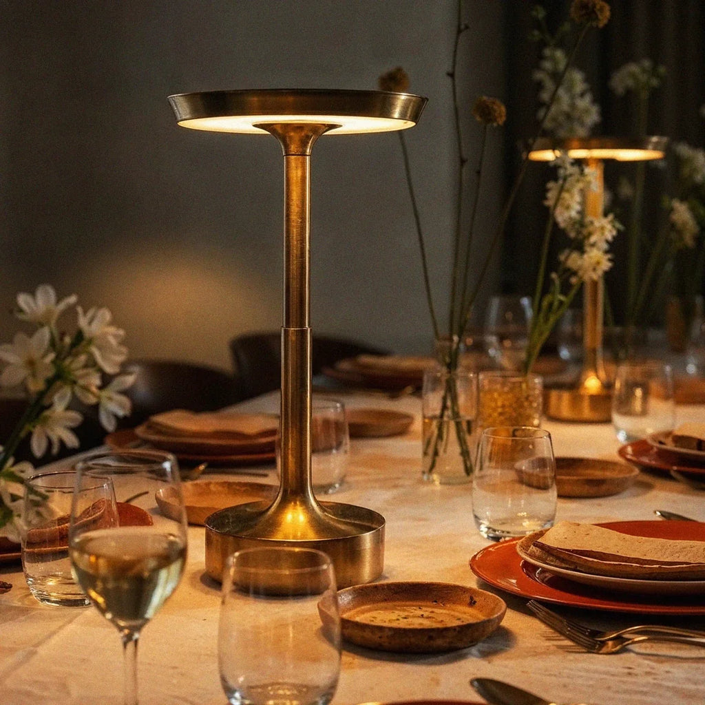 Two lit Clérachic gold table lamps stand along a linen-set dining table with wildflowers and stoneware plates.