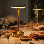 Two lit Clérachic gold table lamps stand along a linen-set dining table with wildflowers and stoneware plates.
