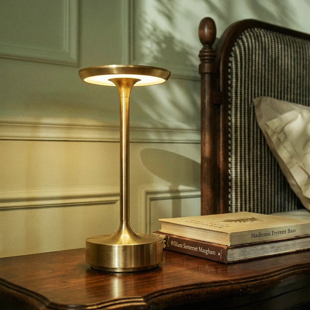 Close-up of the Clérachic gold table lamp glowing beside a stack of books on a dark wood nightstand.
