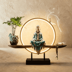 Clérachic incense-burner lamp lit warm, an ornate bronze-teal Guanyin figure beside a potted fern and vase.