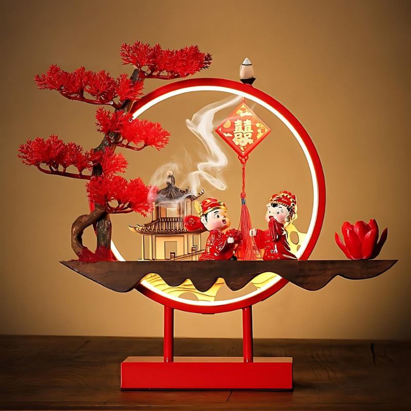 Clérachic incense-burner lamp in red on a wood table, two figures in festive dress under a red tree.