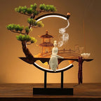 Clérachic incense-burner lamp on a wood table, a standing white figure beside a softly lit pagoda scene.