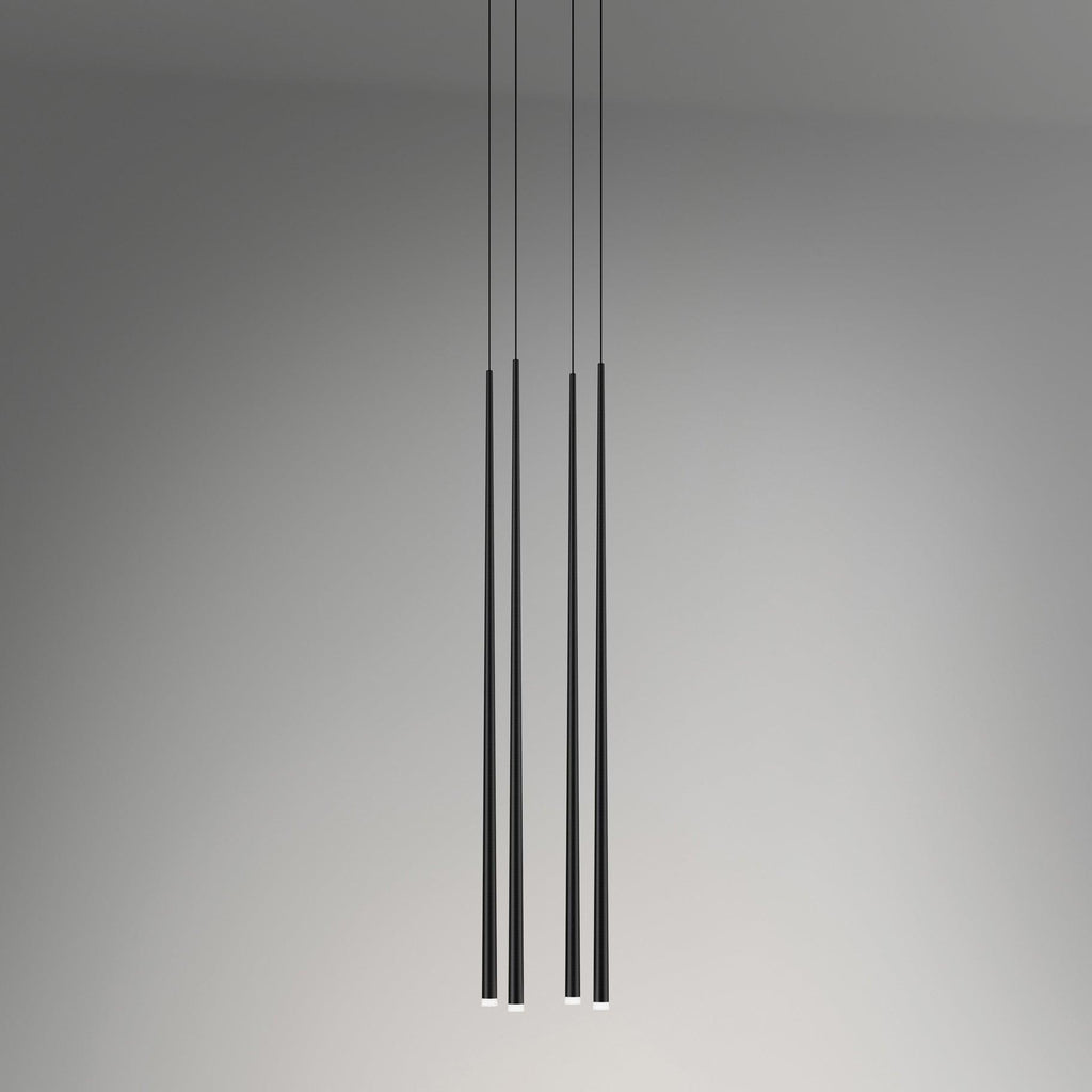 Four black tapered tubes hang at two different drops against a soft grey wall, each tip lit, a Clérachic pendant.