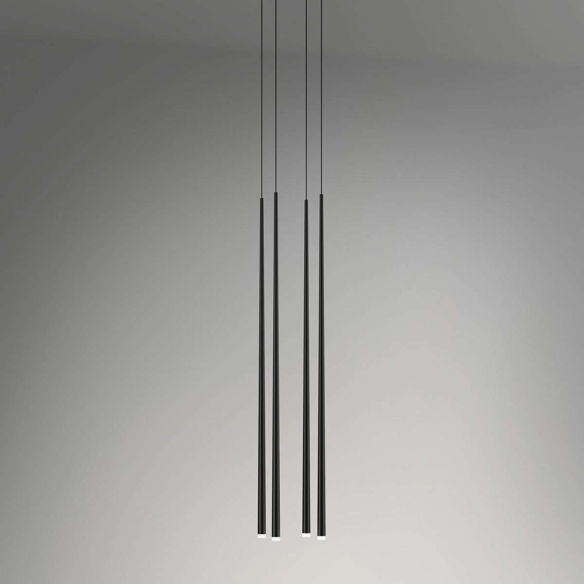 Four black tapered tubes hang at two different drops against a soft grey wall, each tip lit, a Clérachic pendant.