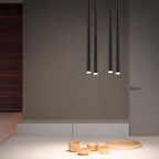 Four black tubes in two pairs hang against a taupe wall above a pale counter with small wooden bowls, a Clérachic pendant.