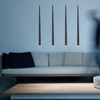 Four black cone-shaped pendants in a line over a pale blue sofa and low wooden table, tips softly lit, a Clérachic pendant.