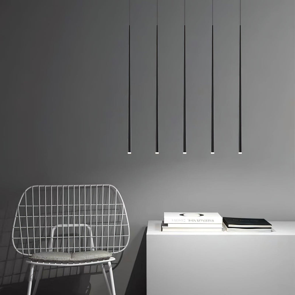Five very long black pendant tubes hang evenly over a white cabinet and a wire chair on a grey wall, from Clérachic.
