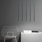 Five very long black pendant tubes hang evenly over a white cabinet and a wire chair on a grey wall, from Clérachic.