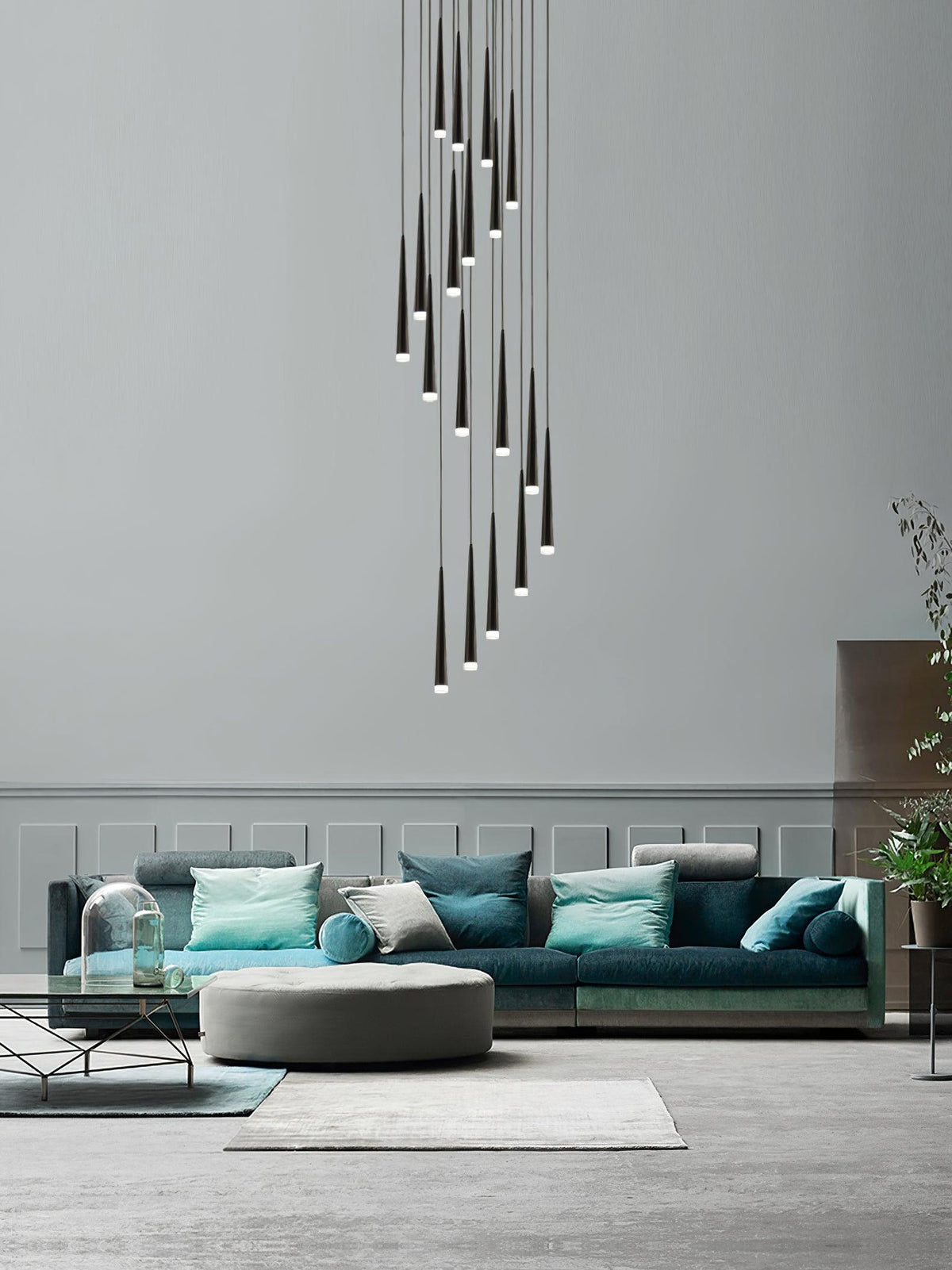 Spiralling cluster of black tapered pendants hangs in a double-height room above a teal sofa and round pouffe, a Clérachic pendant.