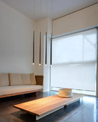 Four black cone pendants hang near a large window above a low timber table and cream sofa, from Clérachic.