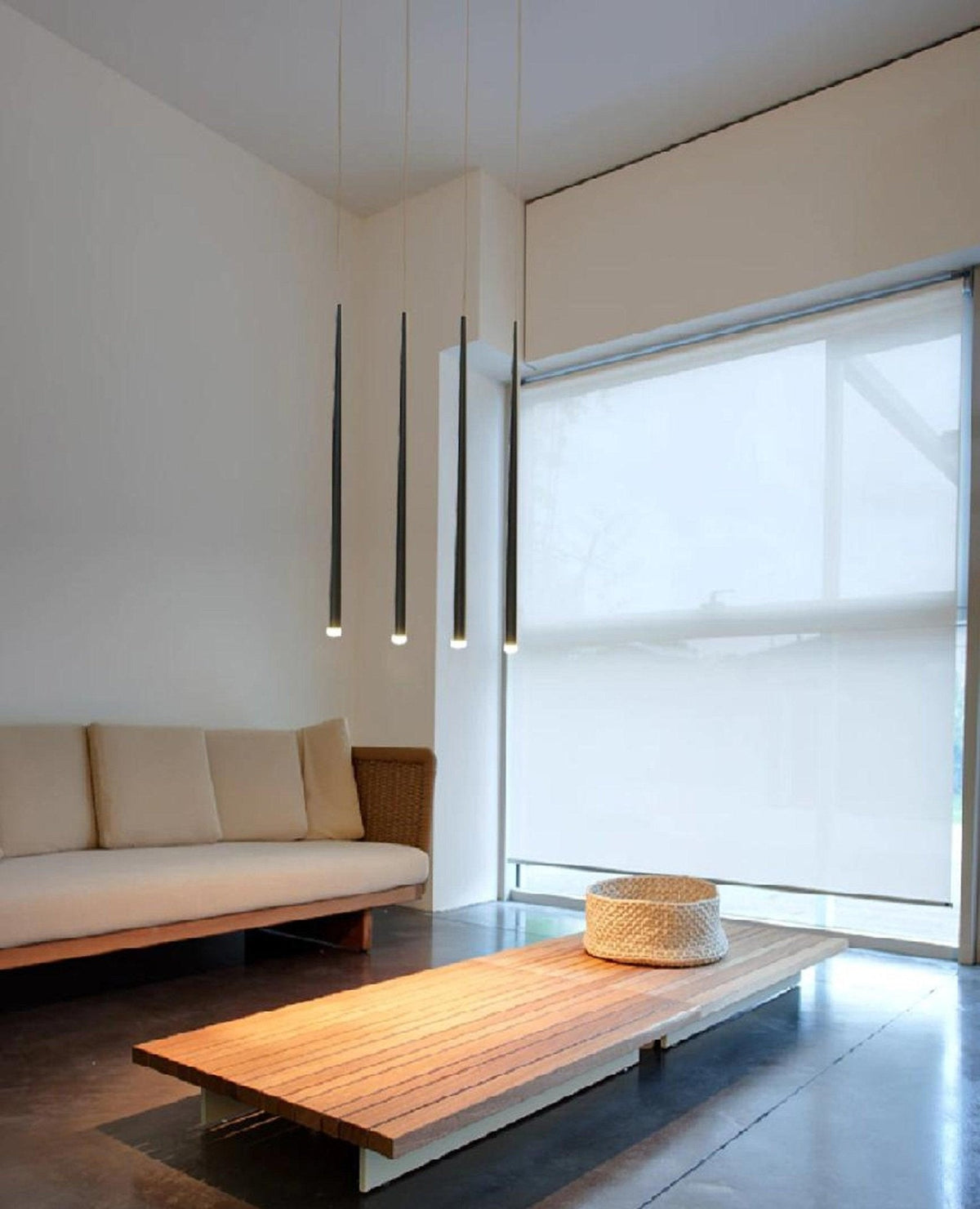 Four black cone pendants hang near a large window above a low timber table and cream sofa, from Clérachic.