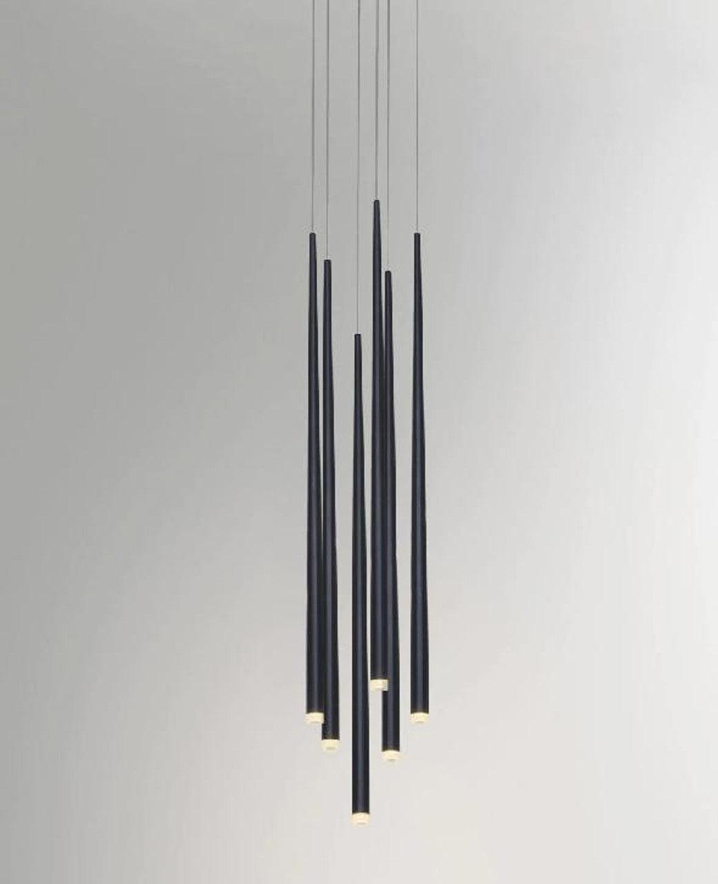 Close grouping of black tapered pendants at staggered lengths against a pale grey wall, tips lit, a Clérachic pendant.