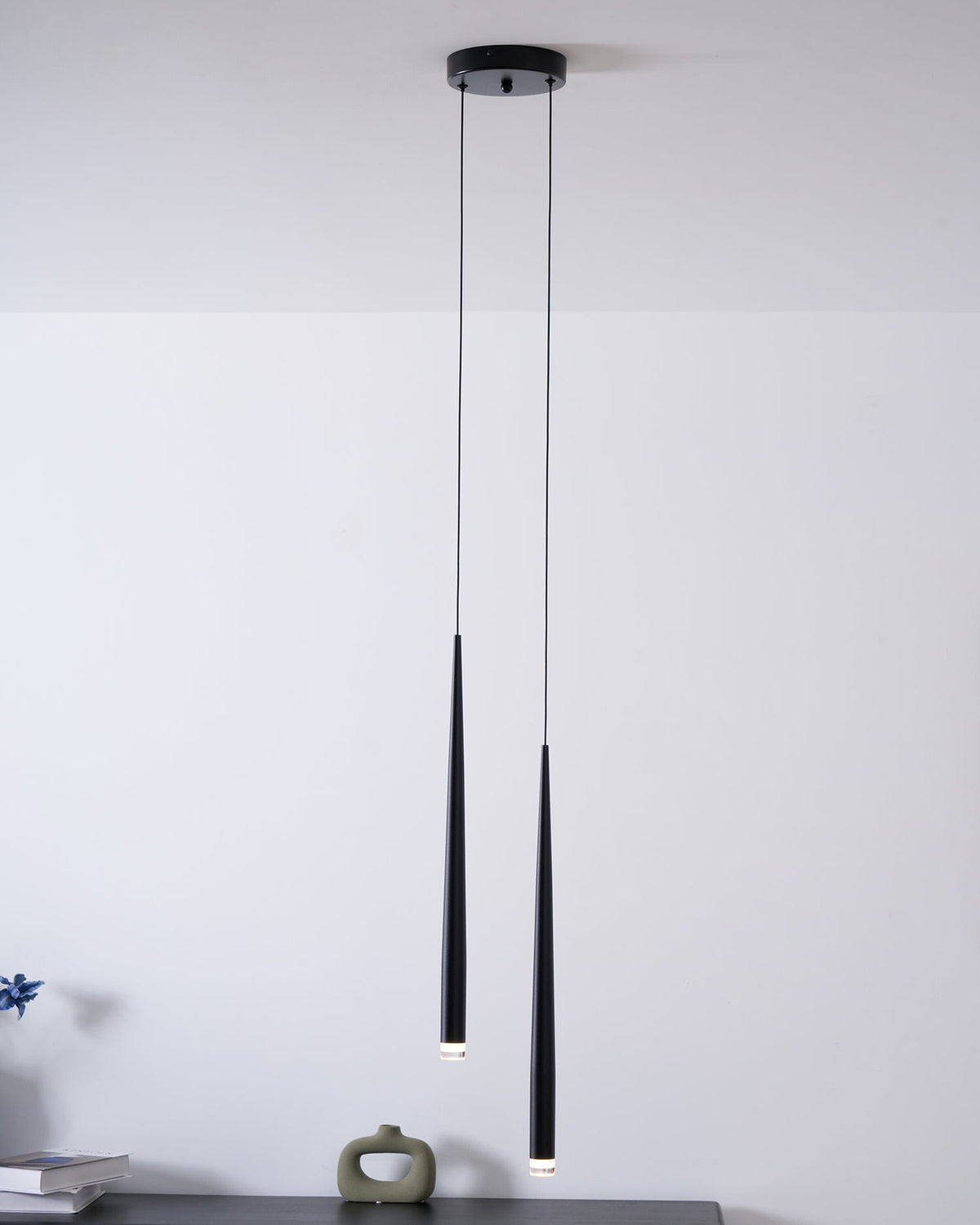 Pair of black cone pendants from a round canopy over a dark console with a small ceramic ornament, a Clérachic pendant.