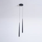 Two black tapered pendants of unequal length hang from a round canopy on a plain pale wall, from Clérachic.