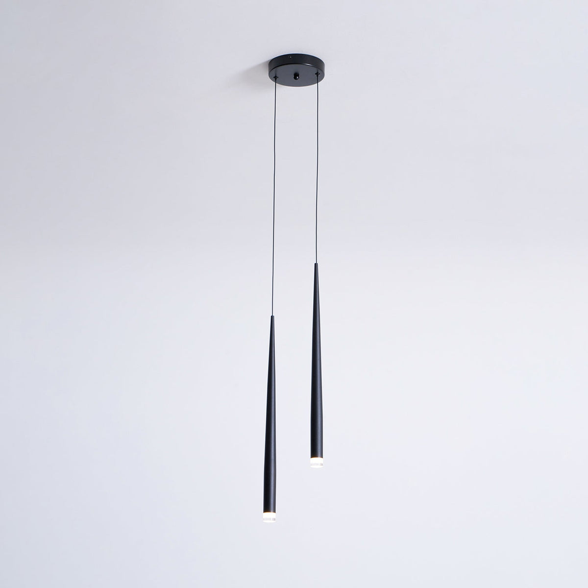 Slim two-light black pendant from a small round canopy, one tube longer than the other, with glowing tips, a Clérachic pendant.
