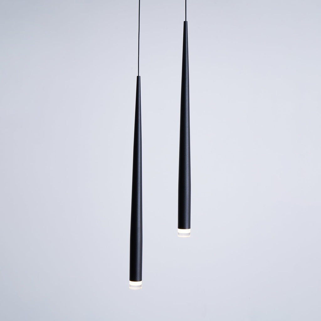 Two black tapered pendants seen close up against a soft grey wall, with the lit tips just visible, from Clérachic.