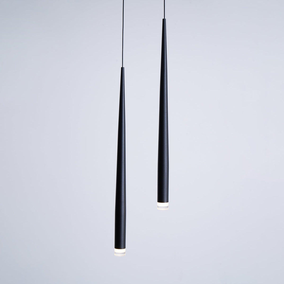 Two black tapered pendants seen close up against a soft grey wall, with the lit tips just visible, from Clérachic.
