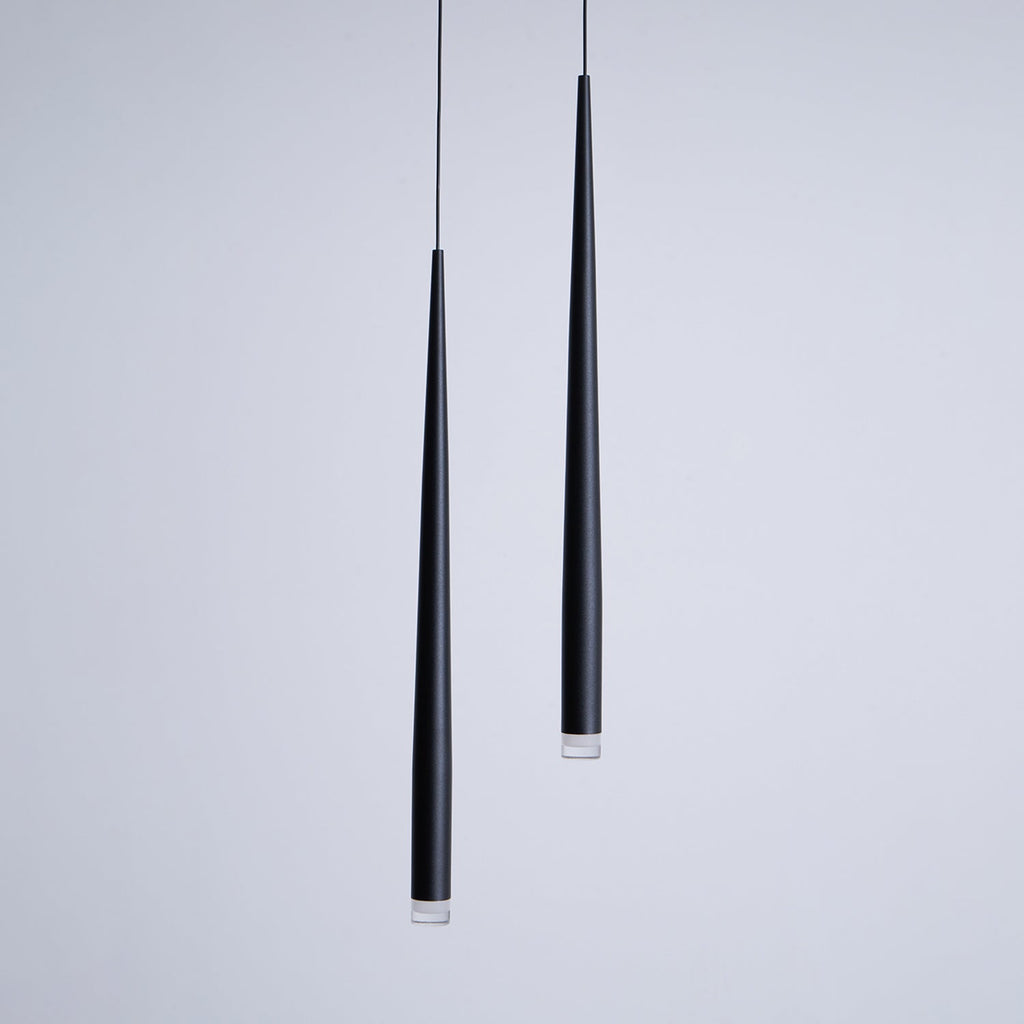 Close view of two black cone pendants at different lengths, matte finish and clear lens at the tips, from Clérachic.
