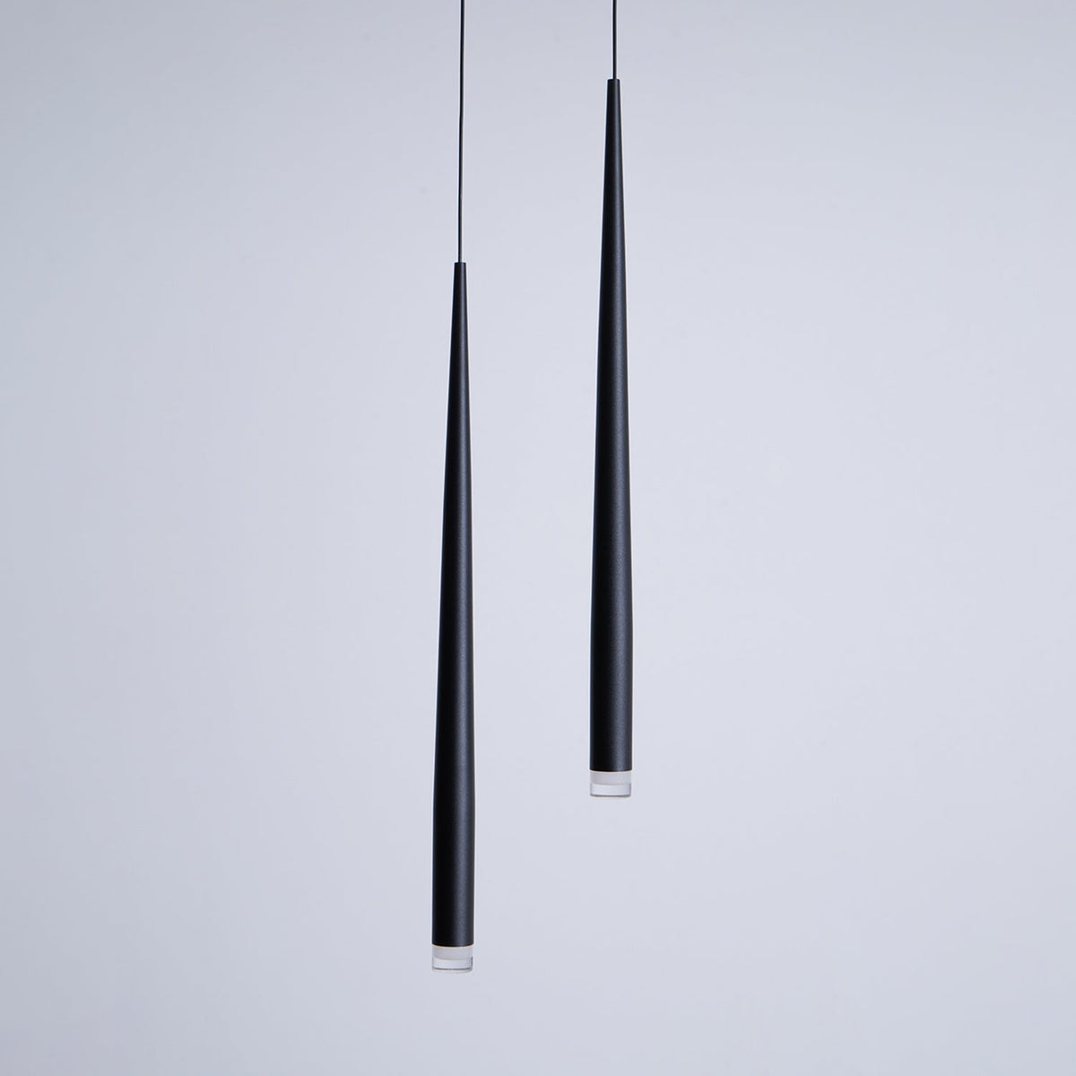 Close view of two black cone pendants at different lengths, matte finish and clear lens at the tips, from Clérachic.